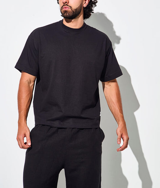 Man wearing a black t-shirt and black pants, standing against a white background.