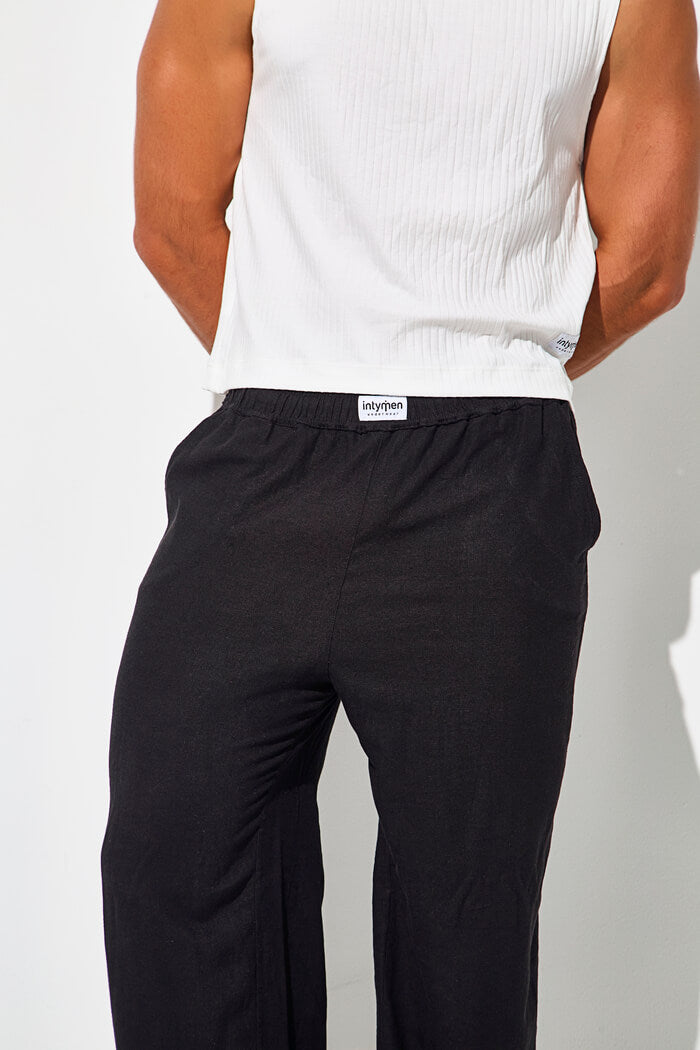 Back view of a man wearing black pants and a white sleeveless top.