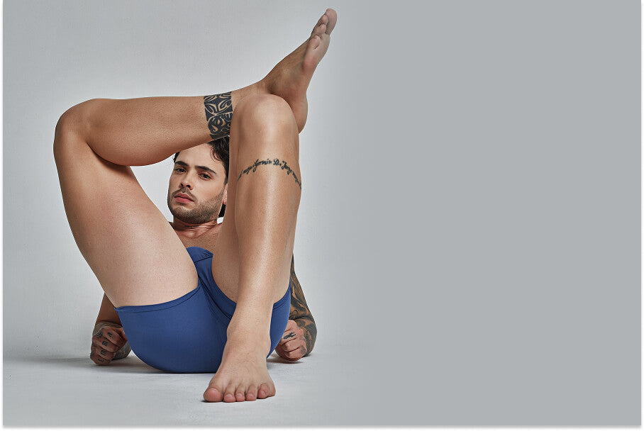 Do You Know These Bizzare Truths About Mens Mesh Underwear? - Man posing on the floor with legs raised, wearing blue underwear.