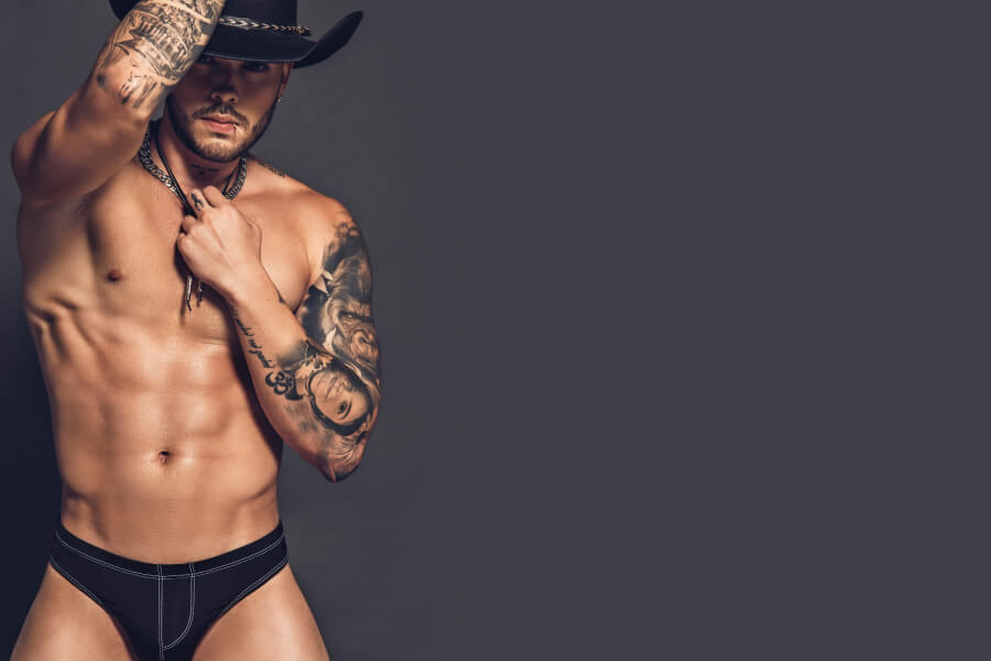 Looking for Mens Jockstraps - Man wearing a cowboy hat and black underwear against a dark background.
