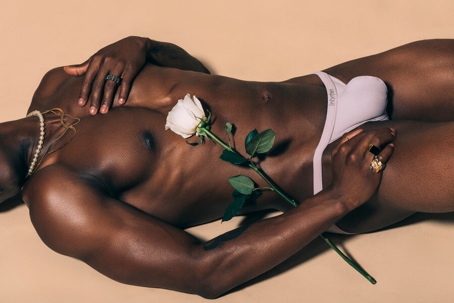 What are the key trends in men's lingerie - Shirtless man in light briefs holding a white rose, adorned with jewelry