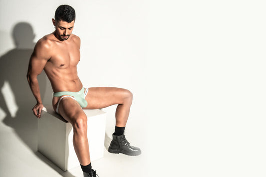 What to Gift the Host this Christmas Party? - Man sitting on a white block wearing mint underwear and black boots.