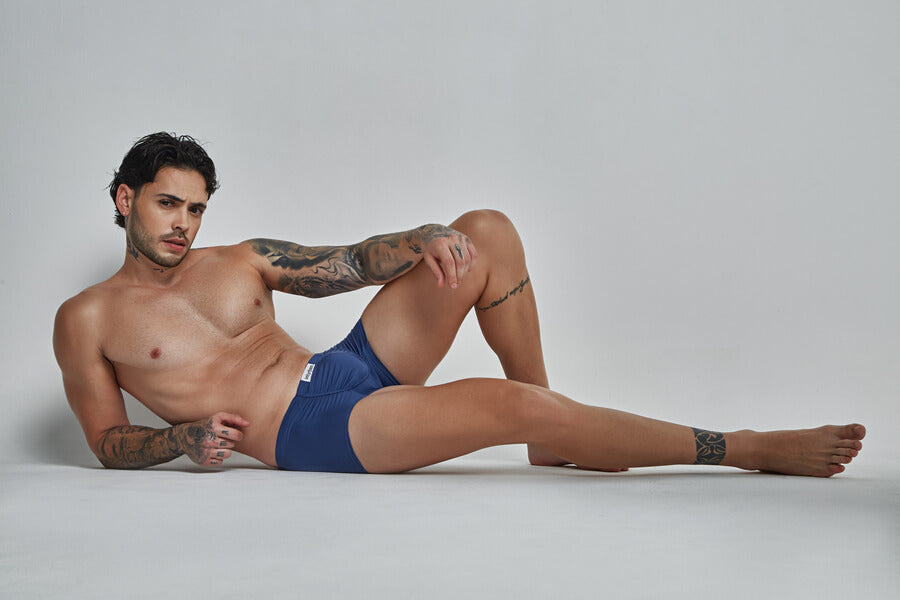 Why do you need a pair of mens thongs -  Tattooed man in navy boxer briefs reclining on a white background